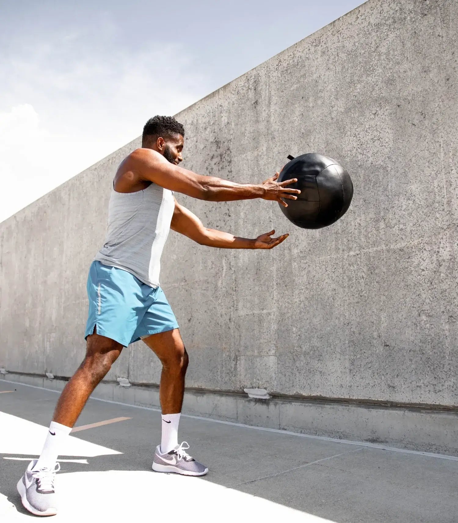 Man exercising outdoors, performing a medicine ball slam for strength training and fitness.
