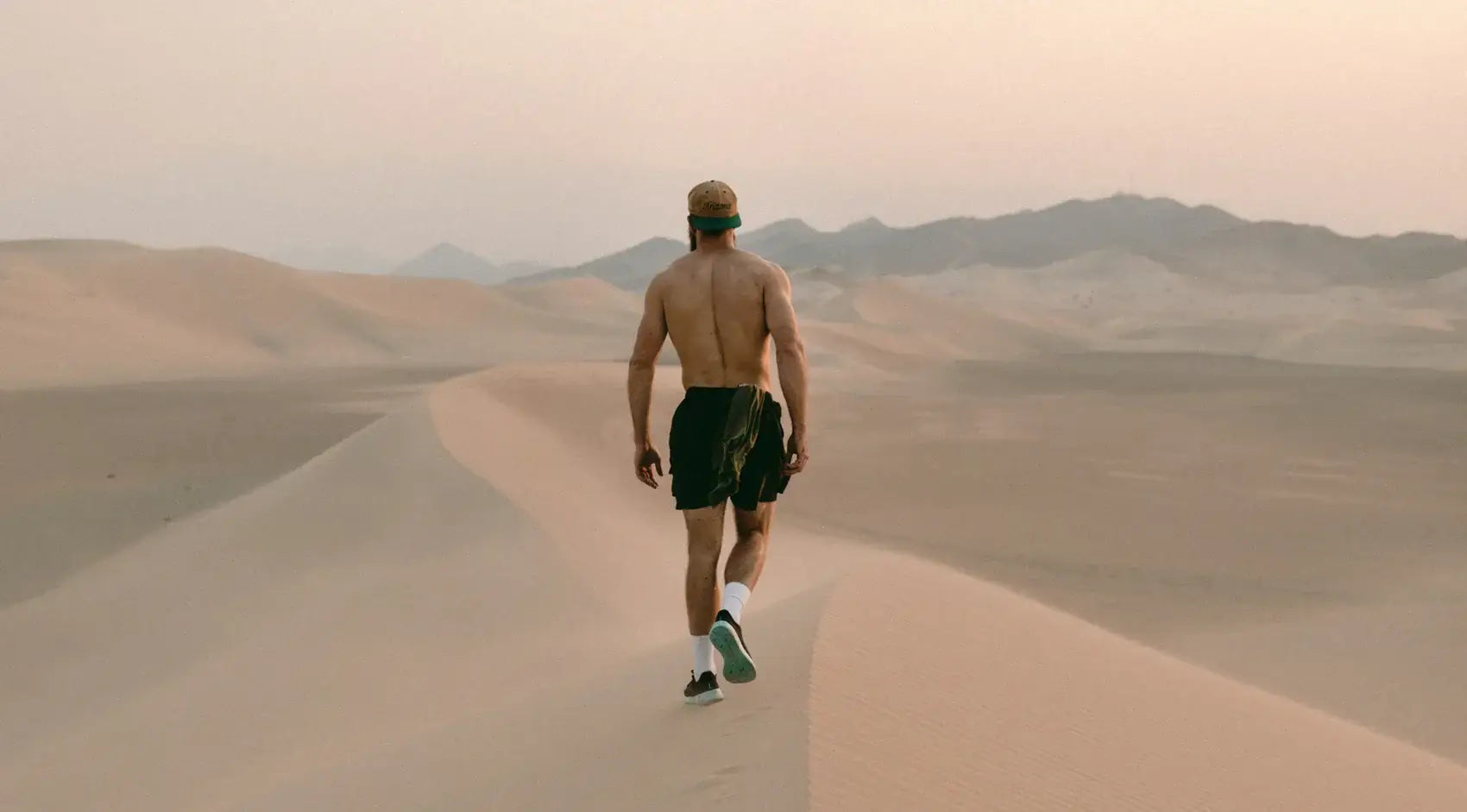 A man walking shirtless in a desert landscape at sunrise, promoting health and outdoor fitness activities.